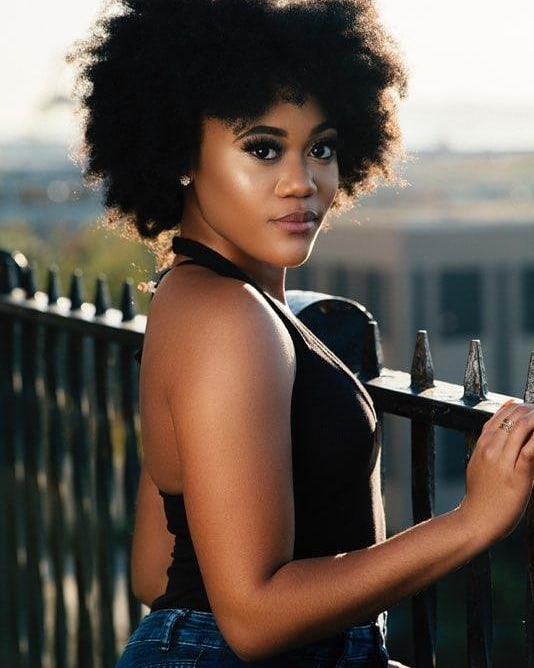 Tyla Harris posing in a black sleeveless top and blue jeans.